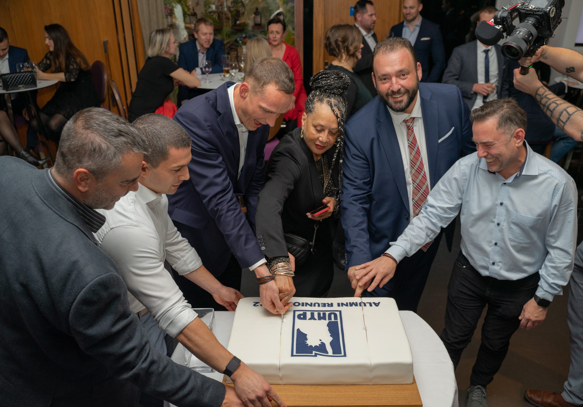 UNYP alumni joyfully cut a reunion cake together at a celebratory event.